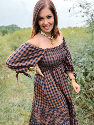 Woman wearing a brown and navy checkered dress in a natural setting