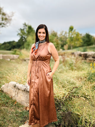 woman wearing Brown faux vegan leather maxi dress with pin tucked cinched waist, functional buttons all the way down front, pockets, and bronze sheen
