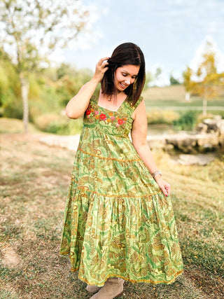 Woman in a green dress with floral patterns standing outdoors in a natural setting.