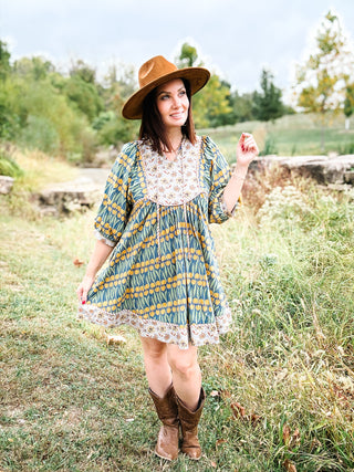 woman in a field wearing Green and Yellow Floral Print with Grey Border and Yoke and Tassel Strings at Split Neckline, styled with a rancher hat and cowboy boots.
