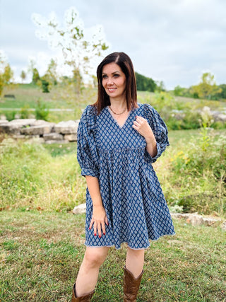Woman wearing a blue patterned dress standing in a grassy outdoor area. Dress is Oversized Blue Geometric Print Babydoll mini dress