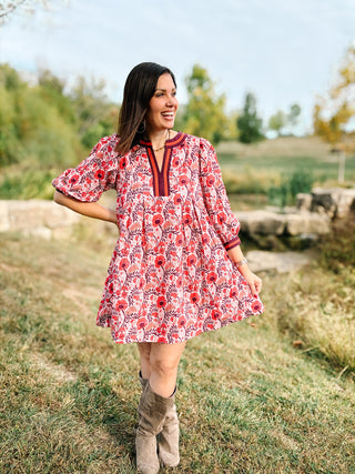 Woman in a floral dress standing in a field with trees in the background. She's wearing Red, Berry, and Rust Floral Fall Mini Dress