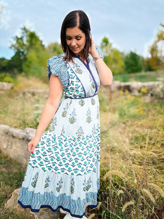 Woman wearing a blue floral and striped patterned maxi dress standing in a natural setting with trees and grass.