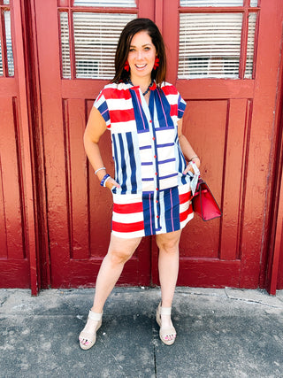 Woman wearing a red, white, navy, and blue mixed stripe button front shirt dress by Alden Adair.