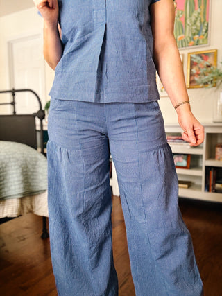 Person wearing a blue striped outfit in a room with a bed and books.