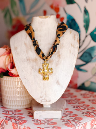 Leopard print necklace with a gold cross pendant on a mannequin bust against a floral background.