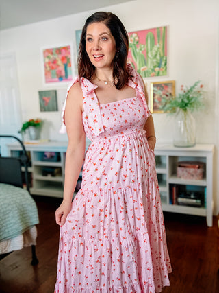Woman in a pink floral dress standing in a room with decor elements.