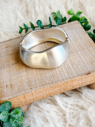 Silver bracelet on a wooden surface with green leaves in the background
