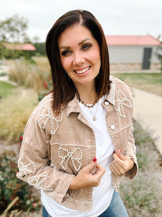 woman wearing a tan corduroy cropped jacket with pearl beaded bow embellishments