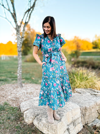 Woman in a floral dress standing on a rock with a scenic background