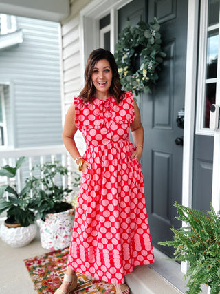 Woman wearing the Annabelle pink polka dot midi dress with a ruffle bib collar, functional button front, neck tie, hidden pockets, and a modest flowy silhouette.