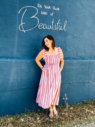 Woman wearing a red and blue striped midi dress with smocked ruffle bodice, tie shoulder straps, and pockets.
