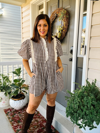 Woman wearing Birdie chocolate brown gingham romper with cream eyelet lace trim, puff sleeves and pockets styled with tall brown boots