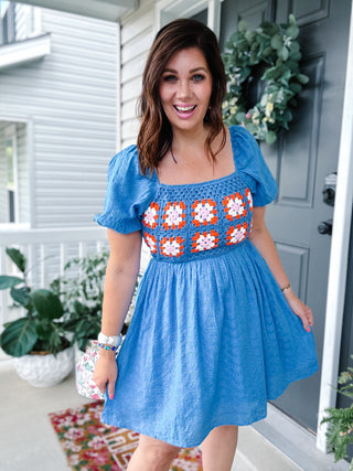 Woman wearing a blue embroidered eyelet mini dress by Karlie with colorful crochet floral trim, puff sleeves, square neckline, and pockets.