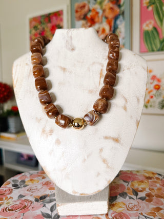 Chunky caramel brown statement necklace with oversized irregular marbled beads in chocolate brown and cream, featuring a polished gold-tone center bead.