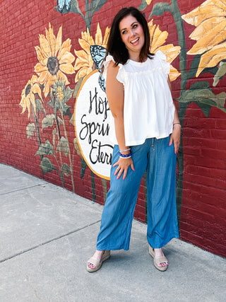 Woman wearing lightweight chambray blue wide leg pants by THML with elastic drawstring waist and pockets.