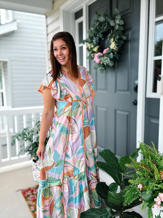 Woman wearing the Ciara tropical print maxi dress with flutter sleeves, colorful watercolor print, lightweight cotton fabric, and flowy tiered silhouette.