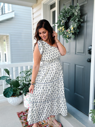 Woman wearing the Francie Midi Dress featuring a blue floral print, one-shoulder neckline, hidden side zipper, tiered midi skirt, and pockets.