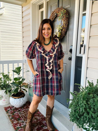Woman wearing Hattie burgundy and navy plaid mini dress with cream lace-trimmed ruffles, puff sleeves and pockets styled with brown cowboy boots