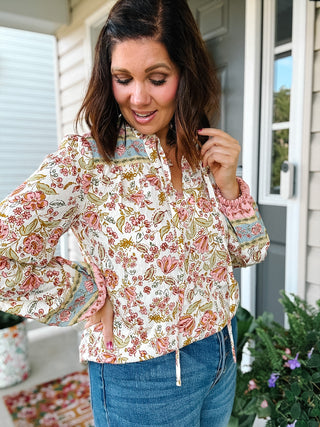 Ivory floral long sleeve blouse with pink flowers, contrast border print, ruffle details and tie neckline.