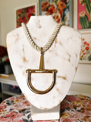 Shop this ivory rope necklace with an oversized gold stirrup pendant. A chic equestrian-inspired statement necklace for preppy and classic outfits.