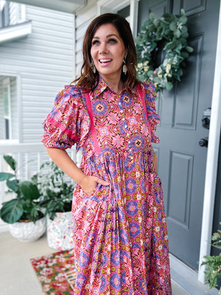 Woman wearing a colorful floral maxi dress by Karlie with lace trim, ruffle shoulders, button-front bodice, puff sleeves, and hidden pockets.