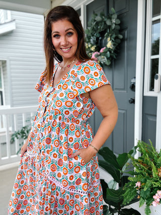 Woman wearing a lavender floral button-front midi dress by Karlie with flutter sleeves, tiered skirt, and a flattering flowy silhouette.