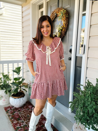 Woman wearing Mabel red and cream gingham mini dress with oversized lace-trimmed ruffle collar, puff sleeves, drop-waist ruffle hem and white cowboy boots