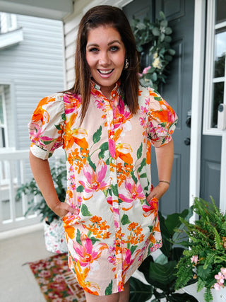 Woman wearing the Magnolia Floral Shirt Dress featuring a colorful watercolor floral print, puff sleeves, button-front design, stand collar, and side pockets.