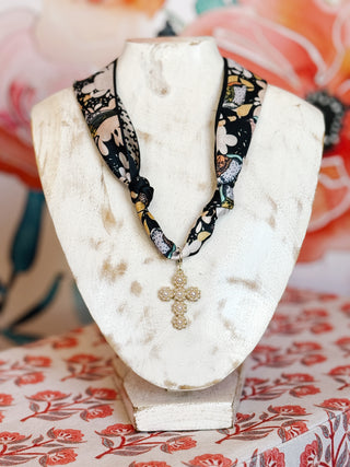 flatlay style photo of a navy floral scarf necklace with gold plated pearl studded cross pendant
