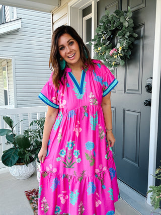 Woman wearing the Parker Midi Dress featuring a bright pink floral print, contrast turquoise trim, flowy midi silhouette, and hidden side pockets.