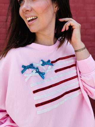 Woman wearing a pink patriotic sweatshirt with glitter bow American flag design and relaxed fit.