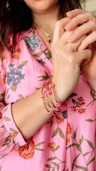 Close-up of a person wearing pink beaded bracelets on a floral dress background