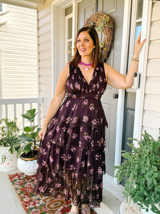 Woman wearing the Daphne plum floral wedding guest midi dress with a plunging V-neckline, defined waist, and cascading tiered ruffle skirt.