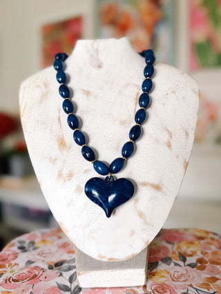 Roxie navy blue beaded statement necklace featuring glossy oval beads, gold-tone spacers, and an oversized marbled navy heart pendant.