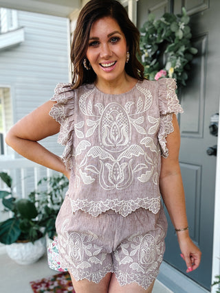 Woman wearing the THML Tamara Embroidered Set featuring taupe textured fabric, ivory embroidery, scalloped lace trim, ruffle sleeves, and matching embroidered shorts.
