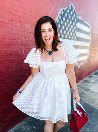 Woman wearing a white textured checkered dress with puff sleeves and a square neckline by Buddy Love.
