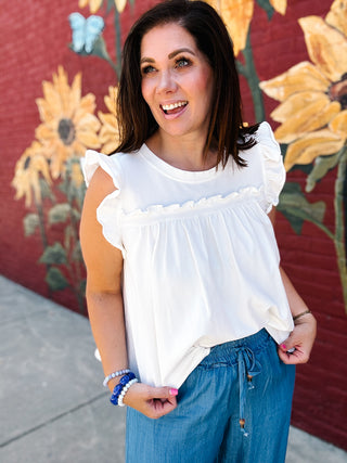 Woman wearing a white ruffle sleeve cotton blend top with a flowy fit and feminine details.