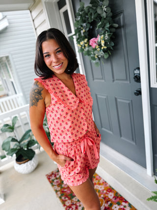Woman wearing the Rebecca coral floral matching shorts set featuring an oversized ruffle sailor collar, button-front sleeveless top, elastic drawstring shorts, ruffle hem, and side pockets.